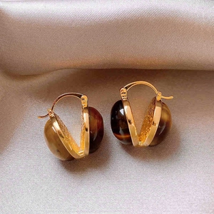 Detail of gold hoop earrings featuring tiger eye stones on a soft satin background