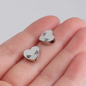 Macro detail of two silver heart-shaped stainless steel beads with wing engraving