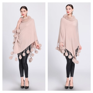 Detail of beige knitted poncho with plush faux fur collar and decorative pompom tassels