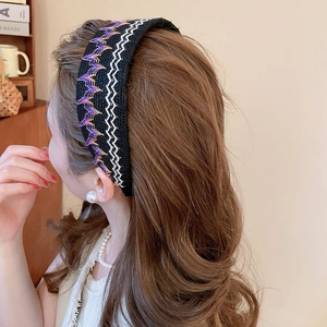 Détail d'un serre-tête noir tissé avec broderie ondulée colorée sur cheveux bruns