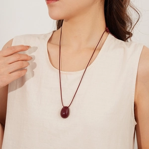 Détail d'un pendentif ovale rouge foncé sur un collier en cordon porté par un mannequin