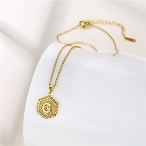 Detail of a golden hexagonal pendant with letter G and beaded edge on white surface
