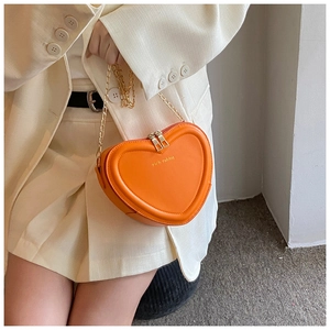 Detail der orangefarbenen Herz-Kettentasche mit goldener Logo-Prägung und Reißverschluss
