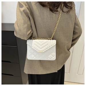 Side view of white quilted crossbody bag with gold chain strap worn by a female model