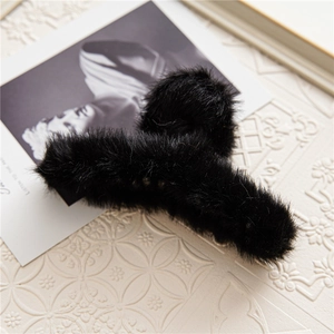 Close-up of black plush hair claw clip with soft faux fur texture on decorative surface