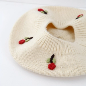 Detailed close-up of cream knit baby beret featuring red and green floral embroidery