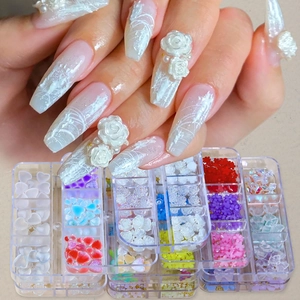 Detailed view of 3D camellia and heart nail charms in a clear compartmentalized box