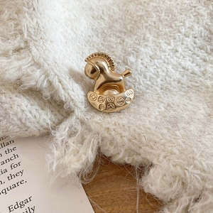 Gros plan d'une broche cheval à bascule dorée épinglée sur un pull en maille beige