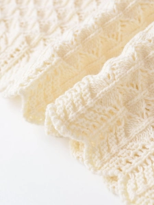 Detail of slim-fit knit top showing intricate hollow diamond weave and scalloped edges