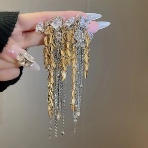 Detail of long tassel earrings featuring golden leaves, silver chains, and square crystals