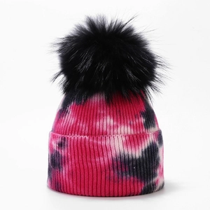 Close-up of tie-dye knit beanie texture with a large fluffy black faux fur pom pom
