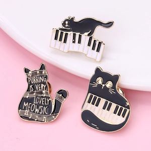 Detailed macro view of black cat piano enamel pins with golden edges on ceramic tray
