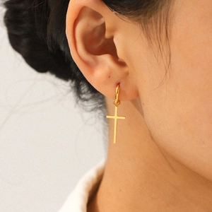 Elegant gold cross dangle earrings in stainless steel worn by a female model