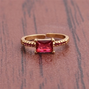 Detail showing an adjustable gold ring with a red rectangular gemstone on a wood texture