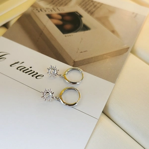 Detail of S925 silver sun earrings with white zircon on a magazine background