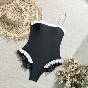 Detail of ruffle trim and white piping on a stylish black one-piece swimsuit flat lay