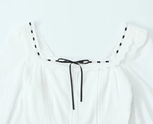 Détail du col carré avec bordure en dentelle et nœud en ruban noir sur une blouse blanche