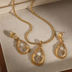 Golden teardrop jewelry set with pearl starburst and textured finish on beige fabric