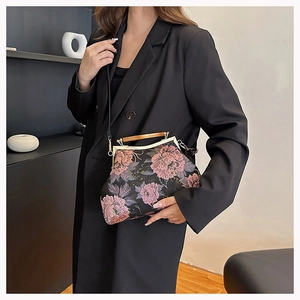 Detail of vintage black handbag with pink floral embroidery and wooden handle on model