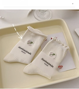 Detail of cream cotton socks featuring delicate purple floral embroidery and wavy edges
