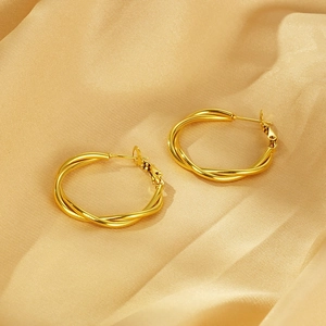 Macro shot of twisted gold titanium hoop earrings on champagne silk fabric background