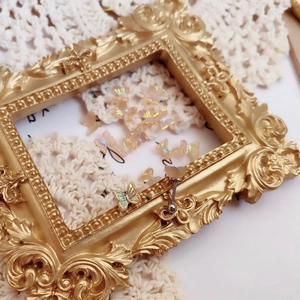 Detailed view of iridescent butterfly stud earring and charms on vintage lace background