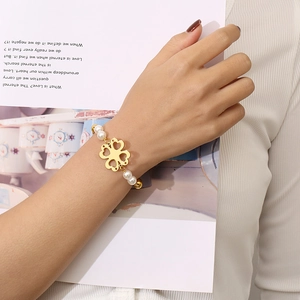 Detail of gold hollow clover charm and white pearls on an elegant charm bracelet