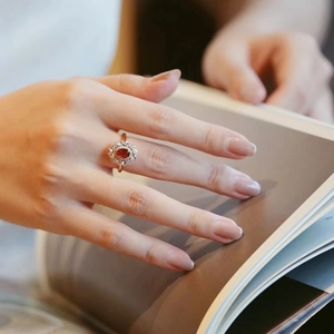 Close-up of elegant rose gold ring with a red ruby gemstone and diamond halo on finger