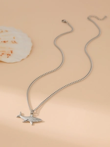 Macro shot of silver shark pendant on Cuban chain with seashell on beige backdrop