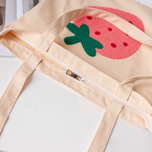 Beige canvas tote bag with 3D strawberry embroidery and a secure metal zipper closure