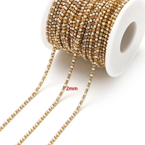 Macro detail of 2mm gold chain with amber rhinestones and pearls on white spool
