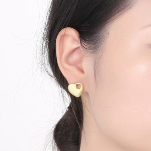 Close-up of a model wearing a golden heart-shaped hollow stud earring made of polished steel