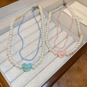 Double-layered pearl choker necklace with pink and blue heart pendants on jewelry box