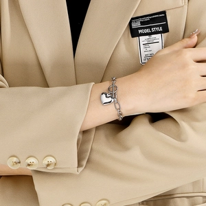 Detail of silver heart charm bracelet with OT toggle clasp on model wearing a blazer