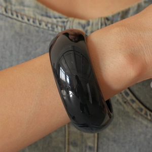 Detail of a wide black resin geometric bangle worn with casual denim clothing
