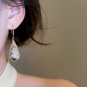 Detalle de pendientes de gota de resina hechos a mano con flores secas reales naturales.
