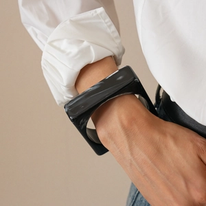 Close-up of a wide square black acrylic bangle with a high-gloss finish on a model wrist