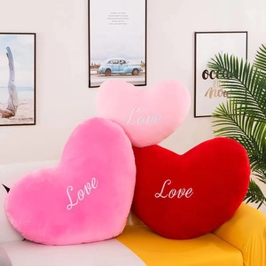 Three plush heart-shaped pillows in pink and red with embroidered Love text on sofa