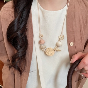 Close-up of bohemian pendant necklace featuring woven rattan disc and geometric wood beads