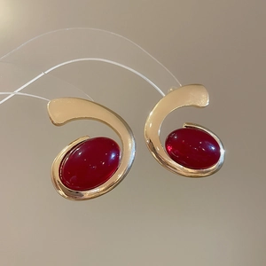 Macro shot of gold metallic earrings with large red oval resin gemstones on reflective surface