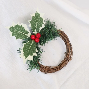 Détail d'une couronne de bougie de Noël avec baies rouges, houx vert et base en rotin