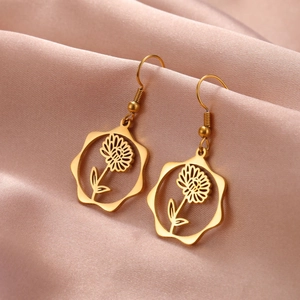Detail of golden flower drop earrings on pink satin showing intricate daisy pattern