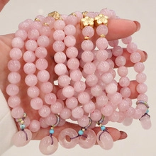 Detailed view of pink quartz beaded bracelets with golden flower and ring charms on hand