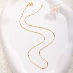 Detail of gold-plated snake chain necklace with lobster clasp on artistic plaster display