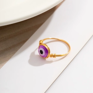 Detail view of handmade gold wire evil eye ring featuring a purple bead and intricate wrap