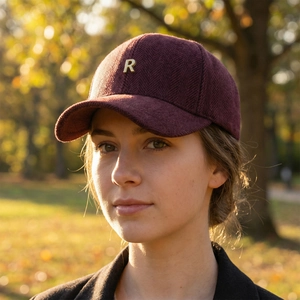 Deep burgundy herringbone baseball cap with metallic R logo worn by a model in autumn