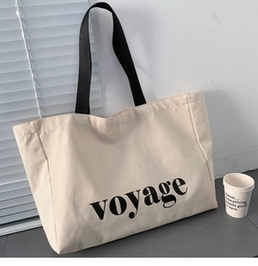 Detail of a large canvas tote bag with black straps and voyage text in natural sunlight