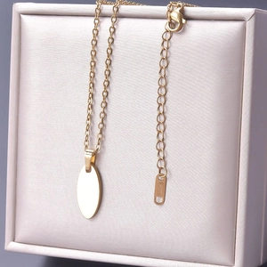 Polished gold stainless steel oval pendant necklace displayed in a beige jewelry box