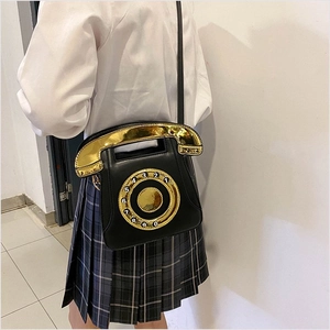 Detail of retro telephone shaped crossbody bag with gold dial worn by a model