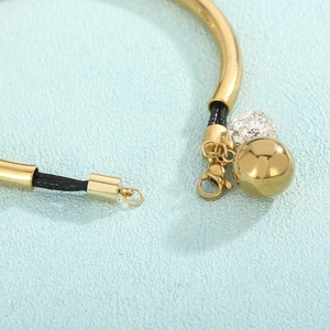 Detail of lobster clasp and gold bead charms on a black braided cord bracelet